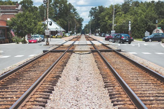 Railroad tracks intersecting through a charming small town with cars and trees.